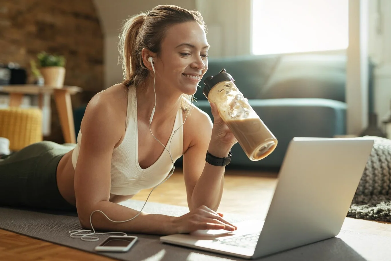 mulher tomando whey protein em frente a laptop